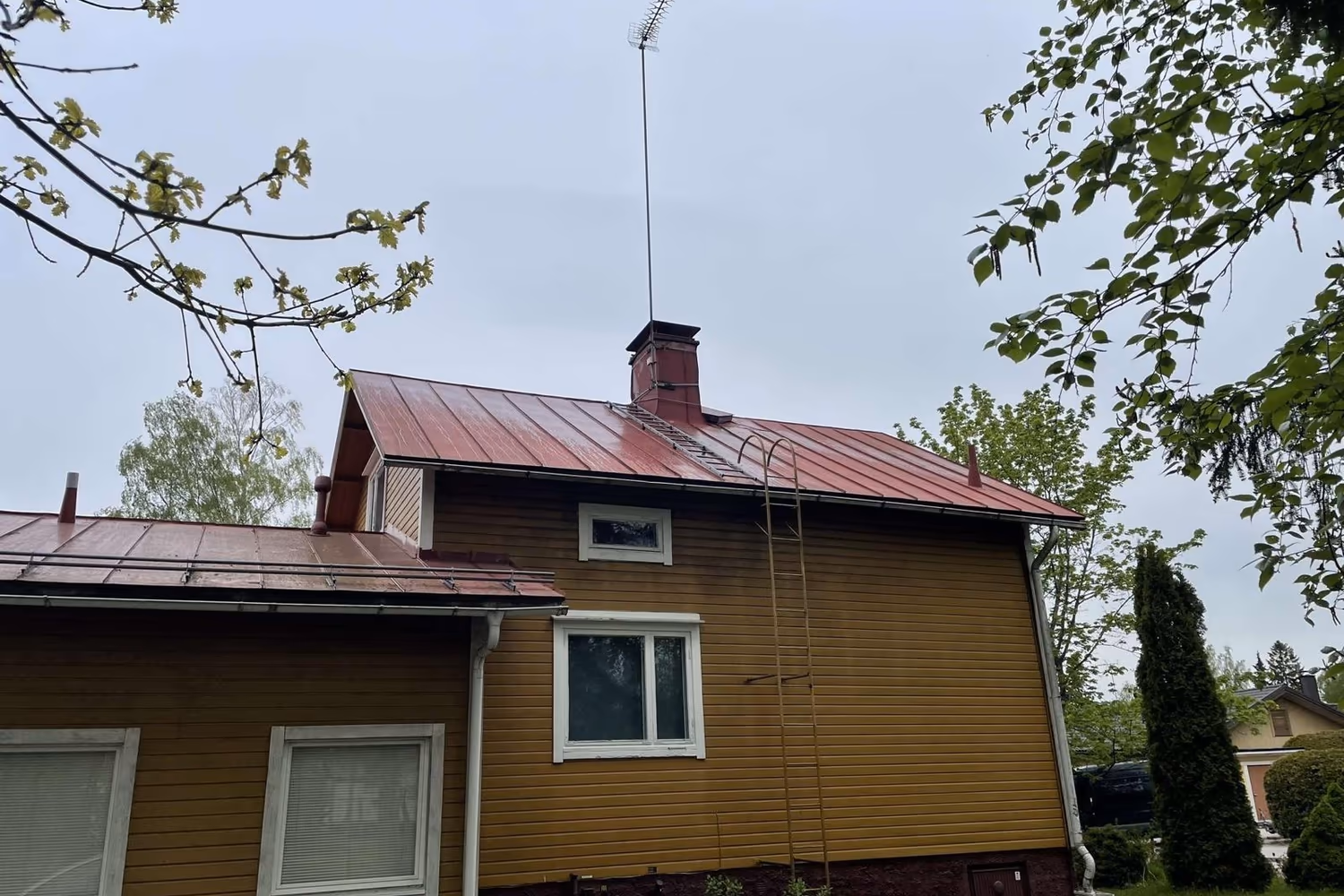 Omakotitalon peltikatto huoltomaalauksen jälkeen, tuore punainen pinta
